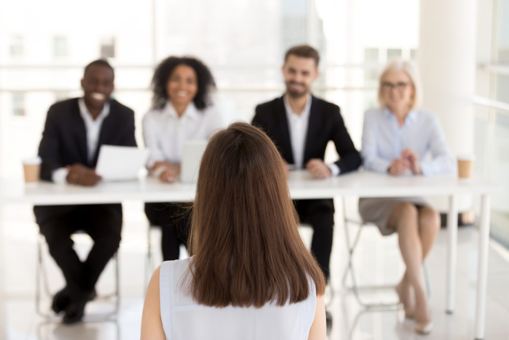 Female job candidate stands before an interview panel during the hiring process.