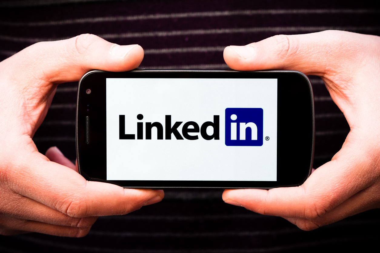 A person holding a cell phone with the LinkedIn logo displayed.