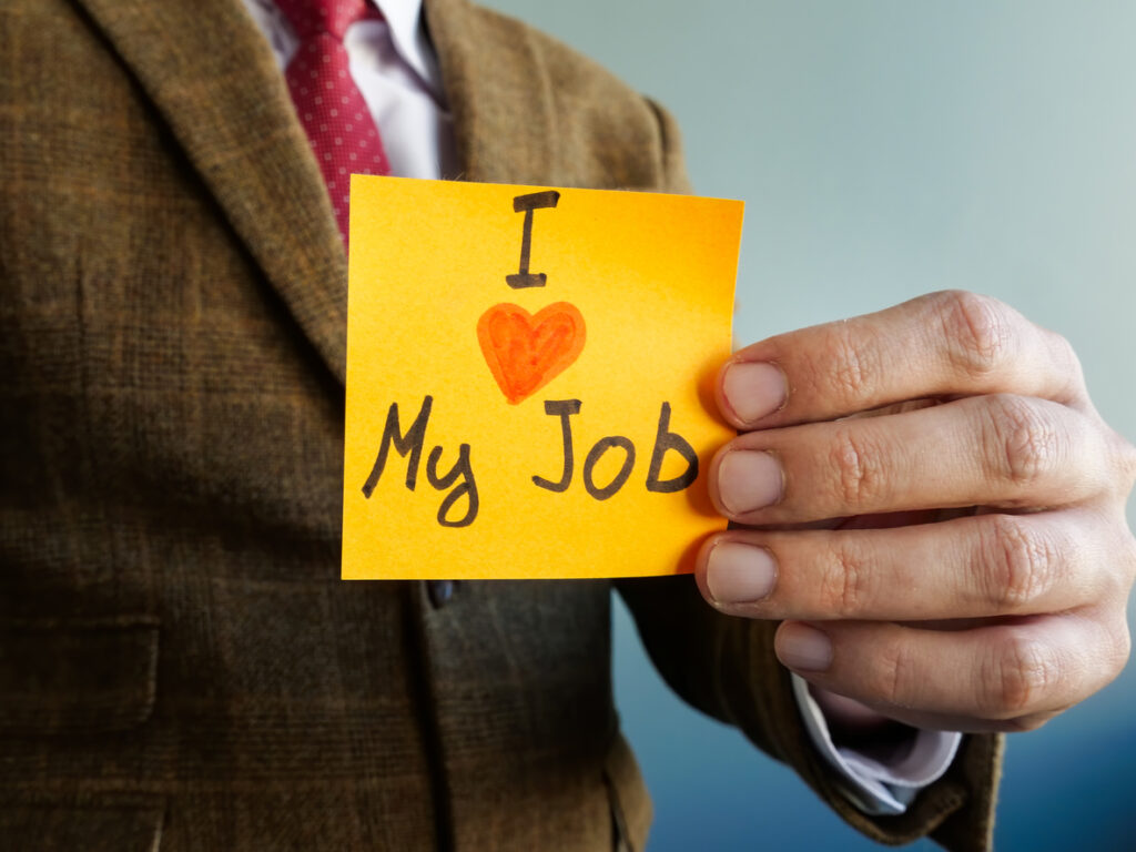 Employee holds sticky note with an "I love my job" message.