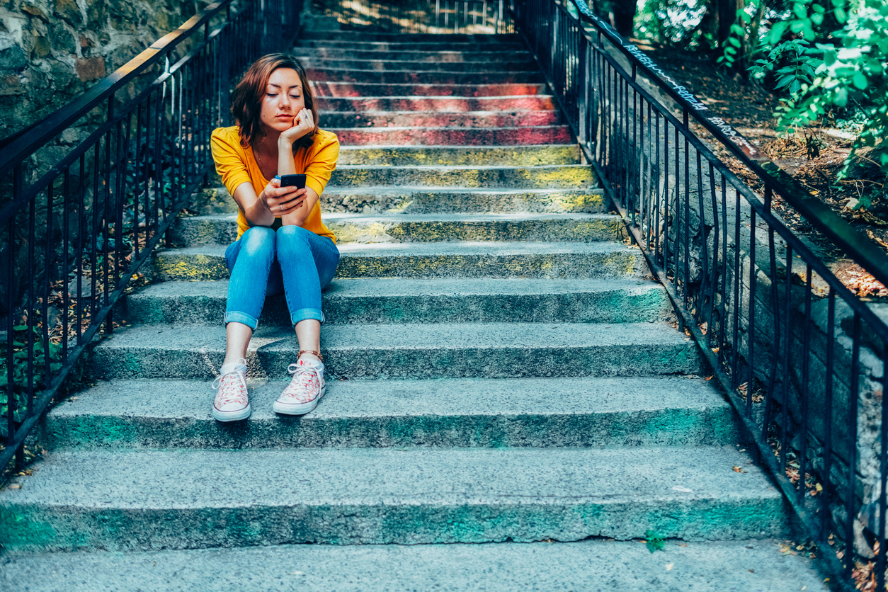 Woman sits on steps looking at her phone after being ghosted.